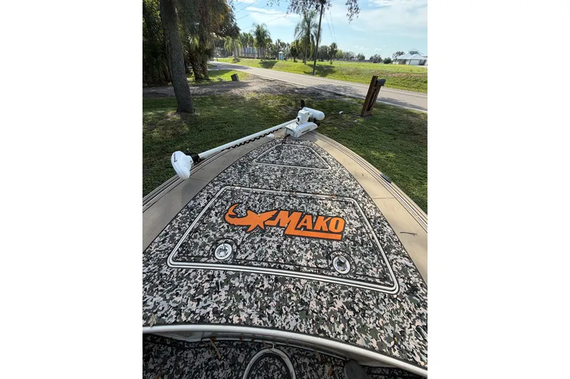Slide: The Image of 2025 Mako 18 Pro Skiff Backwater Edition with camo deck, parked near trees. - 8