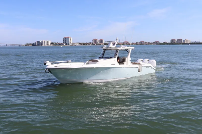 Slide: The Image of 2021 Edgewater 370CC boat cruising on a sunny day near coastal buildings. - 2