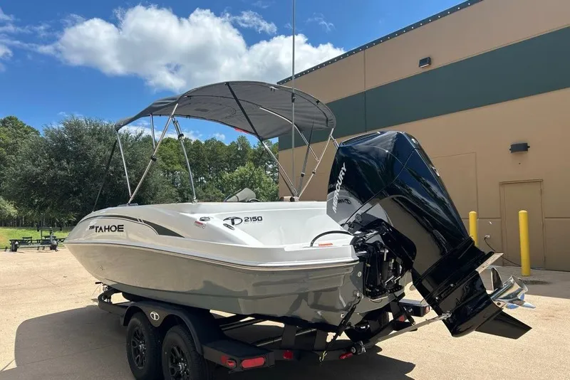 Slide: The Image of 2027 Tahoe 2150 boat with outboard motor on trailer, parked outdoors under blue sky. - 13