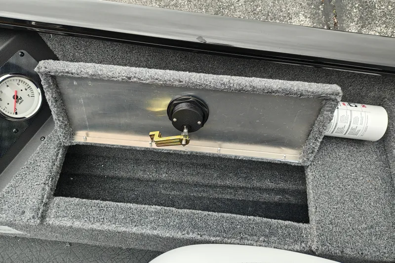 Slide: The Image of Carpeted storage compartment in 2027 Tracker Super Guide V-16 T boat, featuring a gauge and fire extinguisher. - 16