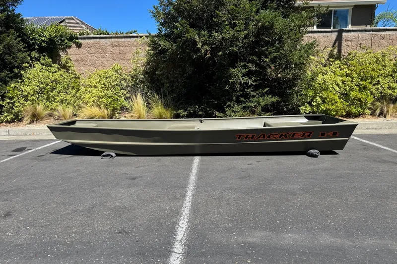 The Image of 2027 Tracker Grizzly 14 Jon boat parked outdoors on asphalt, surrounded by greenery. - 0