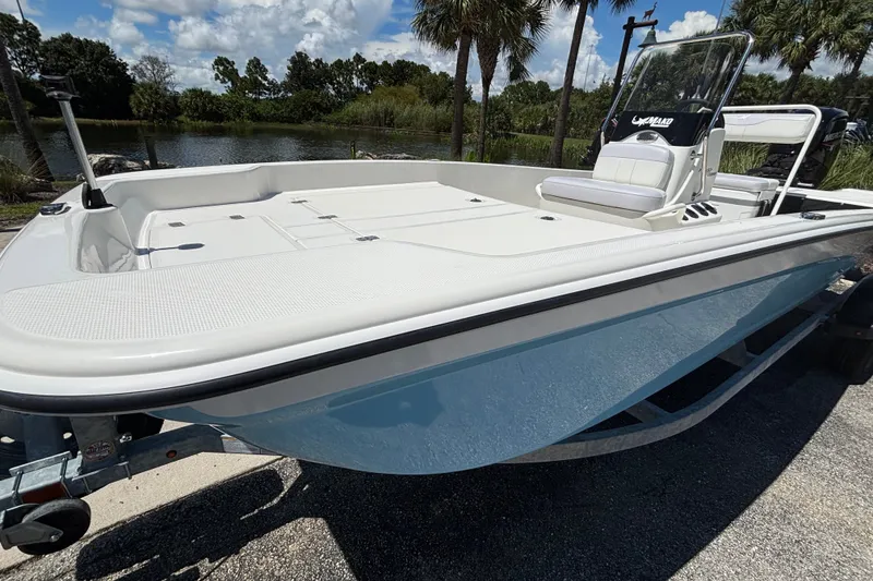 Slide: The Image of 2027 Mako Pro Skiff 17 CC boat on trailer, near a scenic lake with palm trees. - 6