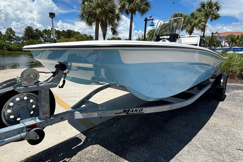 Slide: The Image of 2027 Mako Pro Skiff 17 CC boat on trailer, parked near palm trees. - 2