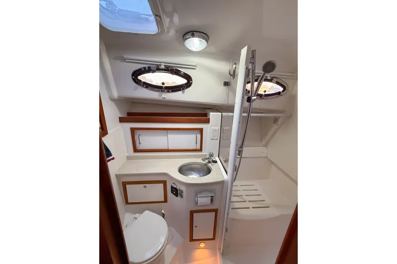 Slide: The Image of 2016 Back Cove 34 yacht bathroom with sink, toilet, and shower, featuring porthole windows. - 32