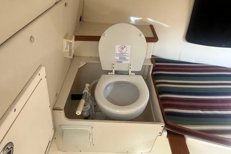 Slide: The Image of 2004 Pursuit 2670 Denali LS boat interior with compact marine toilet and striped cushion. - 16