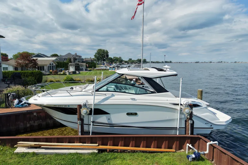 Slide: The Image of 2025 Sea Ray Sundancer 320 docked by a lakeside, under a cloudy sky. - 4