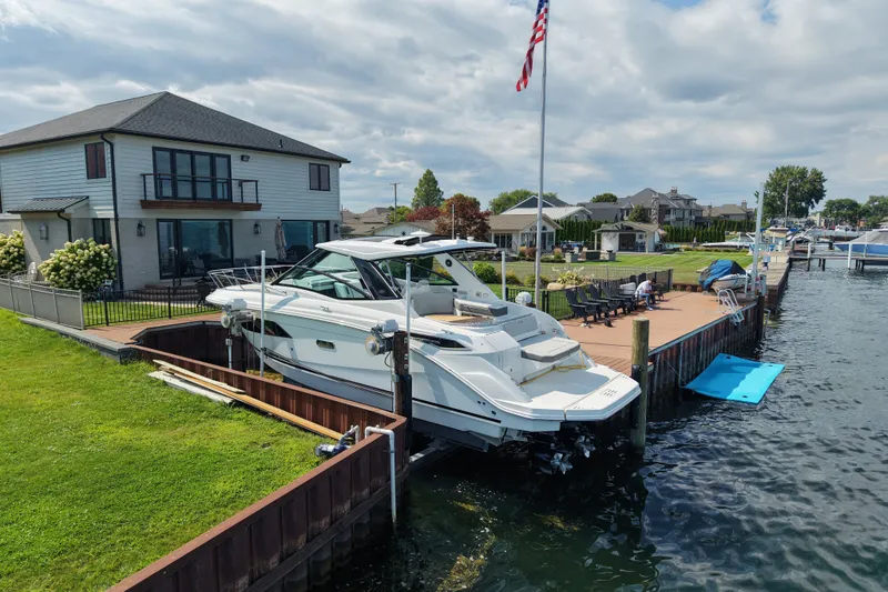 Slide: The Image of 2025 Sea Ray Sundancer 320 docked by a waterfront home under a cloudy sky. - 2
