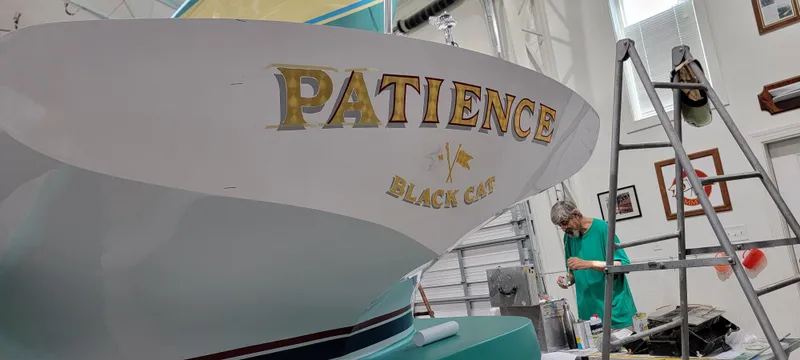 Slide: The Image of Custom M27 boat named "Patience" in a workshop, with a person working nearby. - 8