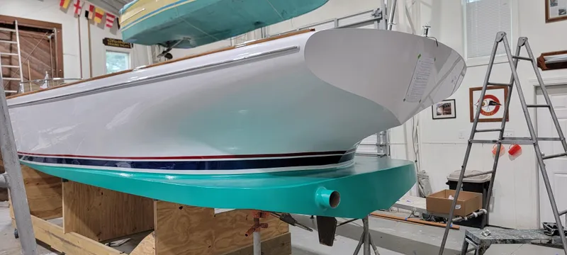 Slide: The Image of Custom M27 boat in workshop, 2023 model, with teal and white hull. - 7