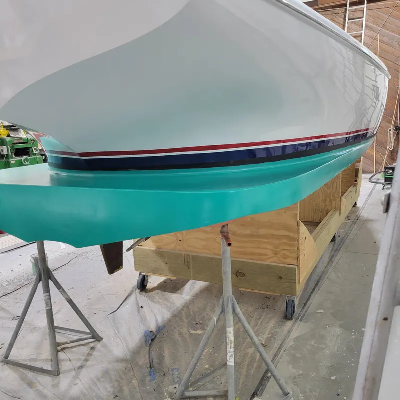 Slide: The Image of Custom M27 boat, 2023 model, with a sleek turquoise hull in a workshop setting. - 12