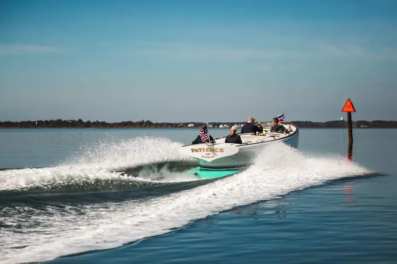Slide: The Image of Custom M27 boat cruising on calm water, 2023 model, with flags and wake trail. - 1