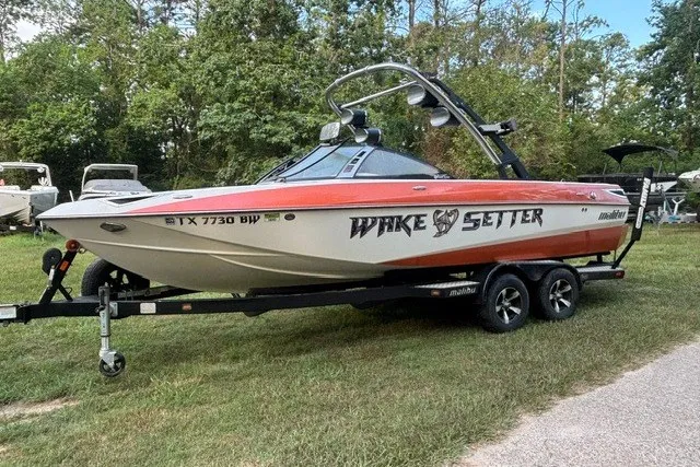 Slide: The Image of 2013 Malibu Wakesetter 23 LSV boat on trailer, parked on grass, surrounded by trees. - 3
