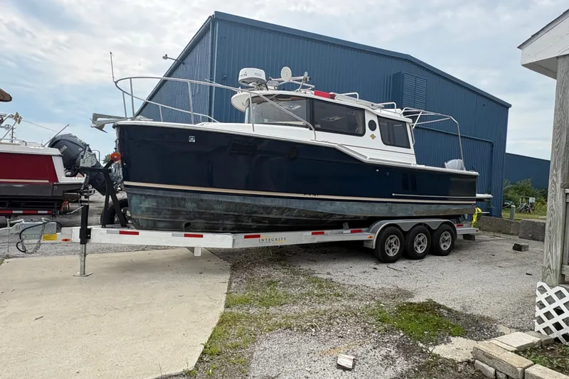 Slide: The Image of 2018 Ranger Tugs R-27 boat on trailer, parked near a blue building. - 2