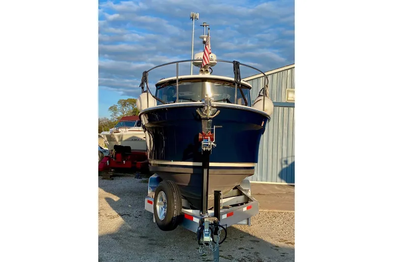 Slide: The Image of 2018 Ranger Tugs R-27 boat on trailer, parked outdoors near a metal building. - 1