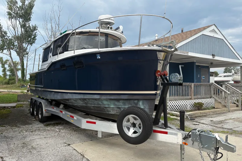 Slide: The Image of 2018 Ranger Tugs R-27 boat on trailer, parked near a house under cloudy skies. - 4