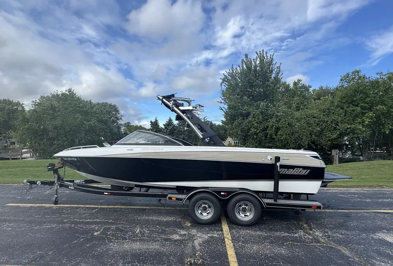 The Image of A 2007 Malibu Wakesetter 23 LSV on a trailer in a parking lot, surrounded by trees. - 0