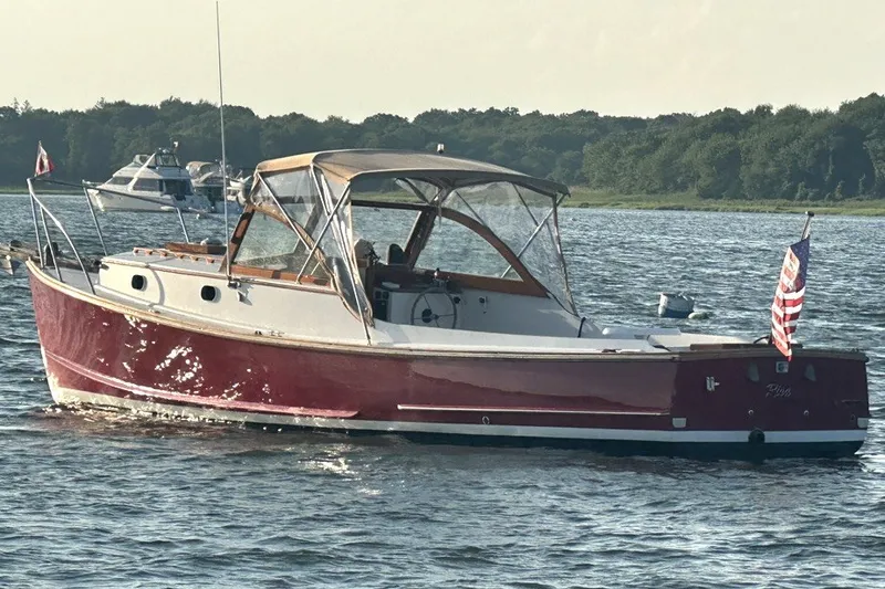 The Image of Classic 1974 Wasque 32 boat with red hull on calm water, featuring a canopy and flags. - 0