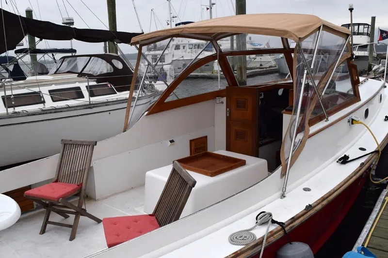 Slide: The Image of 1974 Wasque 32 boat with tan canopy, docked, featuring wooden chairs and red cushions. - 5