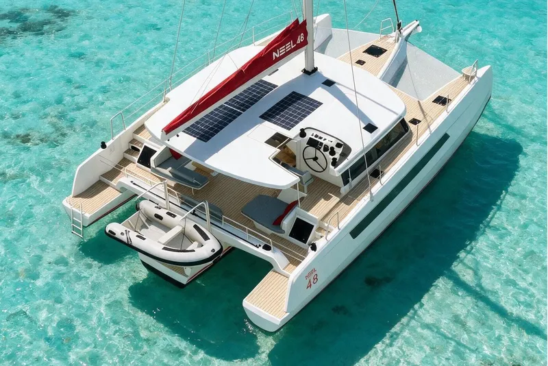 Slide: The Image of 2027 NEEL 48 trimaran sailing on clear turquoise waters, featuring solar panels and a small dinghy. - 1