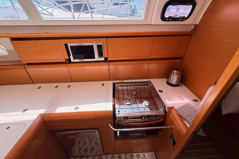 Slide: The Image of Interior of 2014 Jeanneau Sun Odyssey 509 yacht kitchen with stove, microwave, and wooden cabinetry. - 56
