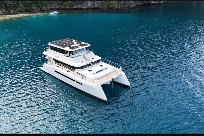 Slide: The Image of 2023 Longreach 58 catamaran cruising in clear blue waters near a rocky shoreline. - 4