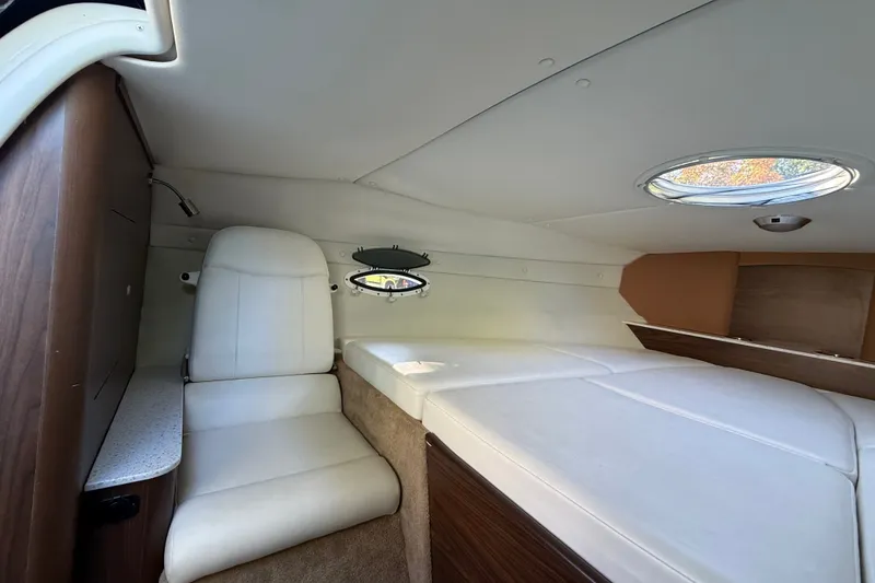 Slide: The Image of 2017 Rinker QX23 CC cabin interior with white seating and a porthole window. - 20