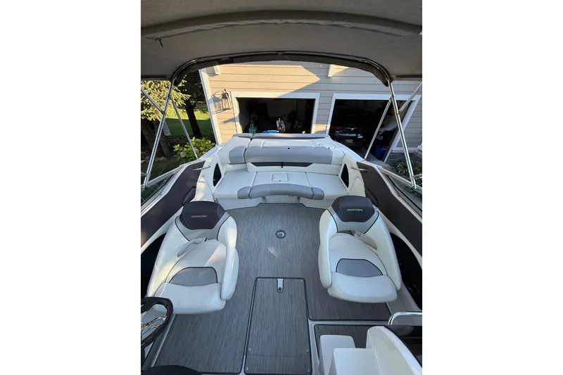Slide: The Image of 2017 Rinker QX23 CC boat interior with seating and canopy in a driveway setting. - 16