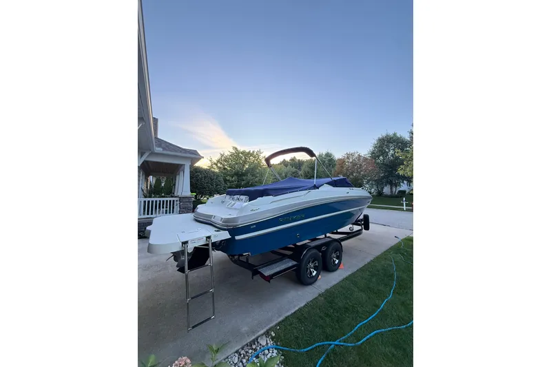 Slide: The Image of 2017 Rinker QX23 CC boat on trailer in driveway, surrounded by greenery. - 24