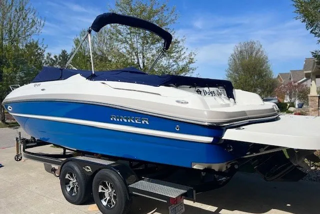 Slide: The Image of 2017 Rinker QX23 CC boat on trailer, blue and white, parked outdoors. - 2