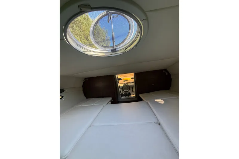Slide: The Image of Interior cabin of 2017 Rinker QX23 CC boat with circular window and white seating. - 22