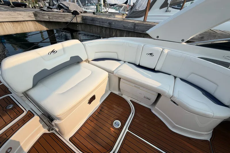 Slide: The Image of 2013 Monterey 264FSX boat interior with white seating and teak flooring at a marina. - 5