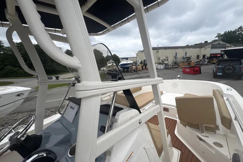 Slide: The Image of 2025 Bayliner Trophy T22CC boat interior with seating and steering console, parked outdoors. - 13
