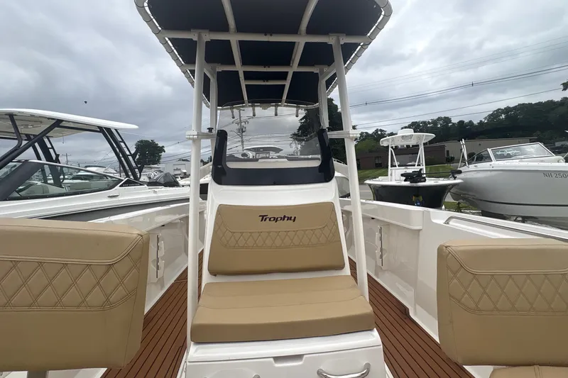 Slide: The Image of 2025 Bayliner Trophy T22CC boat interior with tan seating and T-top under cloudy sky. - 18