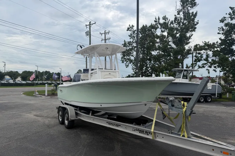 The Image of 2022 Sea Hunt Ultra 219 boat on trailer, parked outdoors with trees and flags in background. - 1