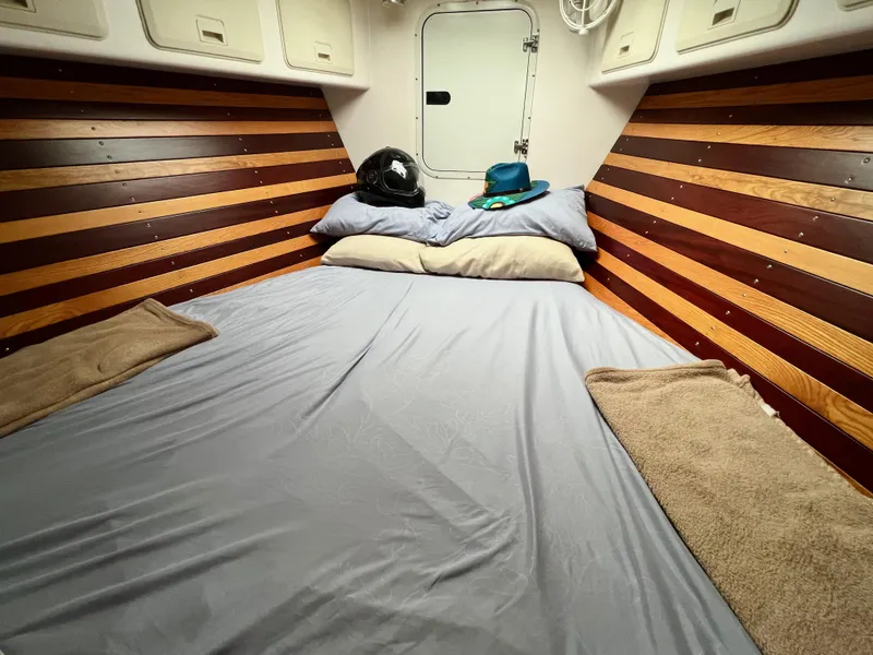 Slide: The Image of Kabine mit gestreiften Holzwänden, einem Doppelbett mit blauer Bettwäsche und Kissen, und einer Tür im Hintergrund. - 25