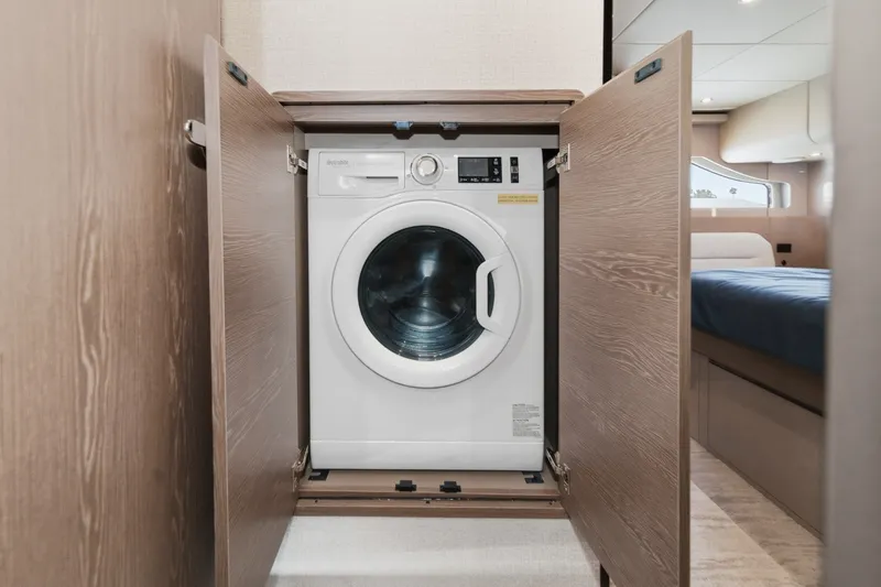 Slide: The Image of Washing machine inside 2027 Cruisers Yachts 50 Fly, with open wooden cabinet doors. - 81