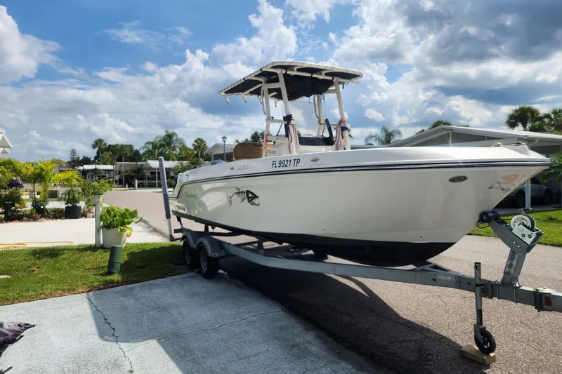 Slide: The Image of 2024 Bayliner Trophy T22CC boat on trailer, parked in a residential area under a cloudy sky. - 0