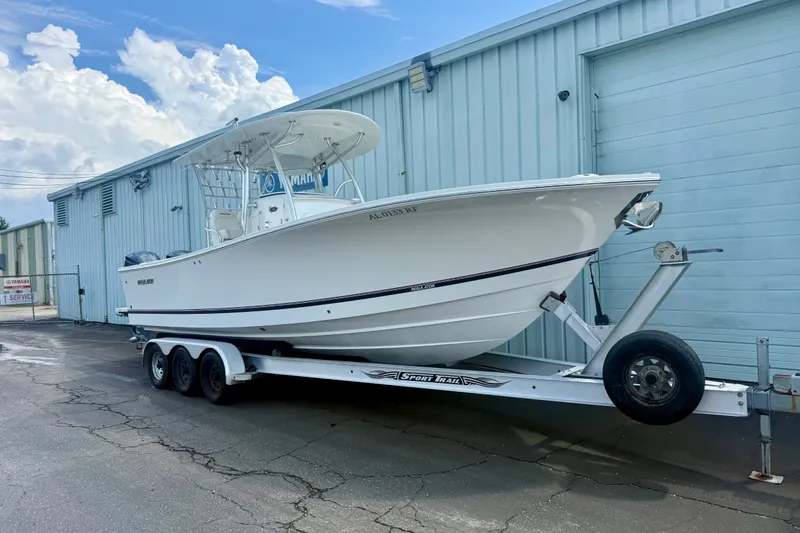 The Image of 2014 Regulator 28 Forward Seating boat on trailer, parked by a blue industrial building. - 0