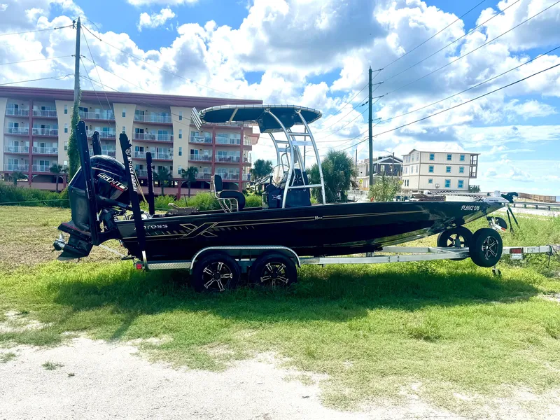 The Image of A 2026 Xpress H22 boat on a trailer, parked on grass with residential buildings in the background. - 0
