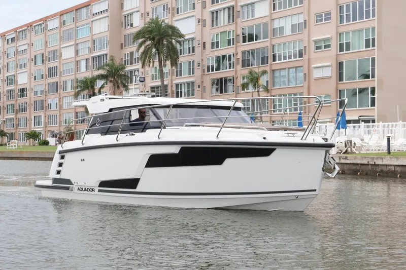 Slide: The Image of 2024 Aquador 300 HT boat cruising near waterfront apartments. - 0