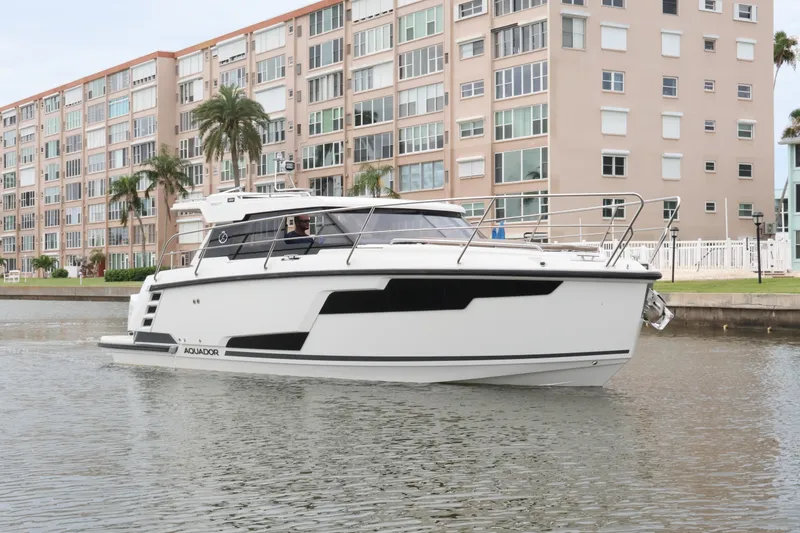 Slide: The Image of 2024 Aquador 300 HT boat cruising near waterfront apartments. - 1