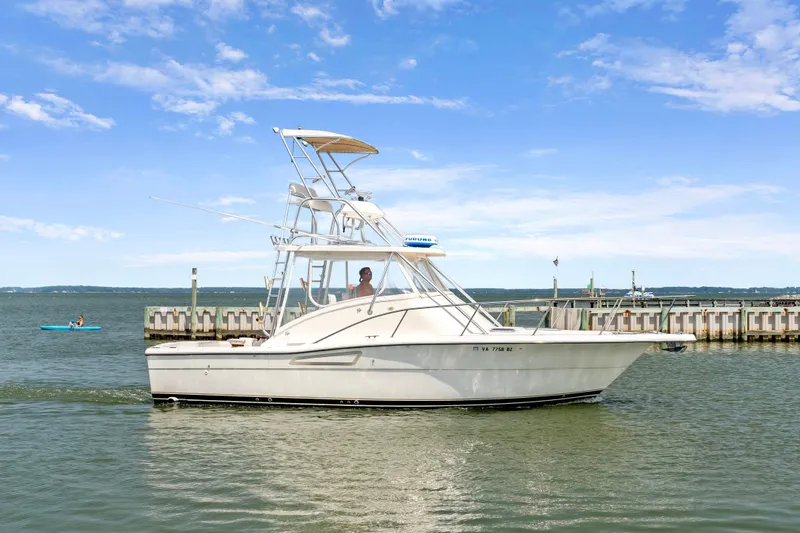 Slide: The Image of 1995 Pursuit 3000 Offshore boat cruising near a dock under a clear blue sky. - 48