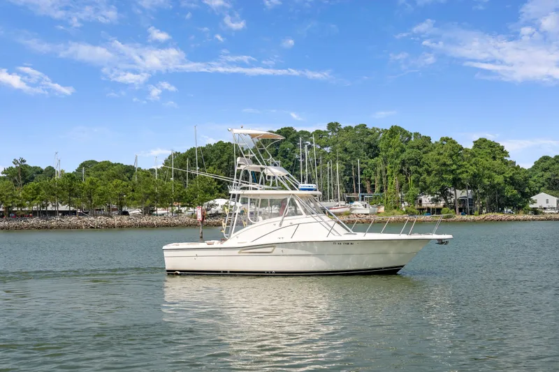 Slide: The Image of 1995 Pursuit 3000 Offshore boat on calm water, surrounded by lush greenery and clear blue sky. - 55