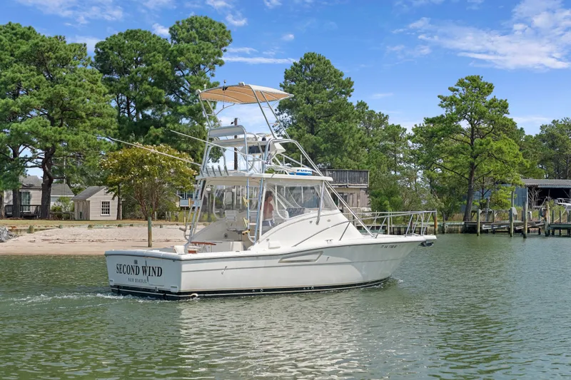 Slide: The Image of 1995 Pursuit 3000 Offshore boat on calm water near a wooded shoreline. - 58
