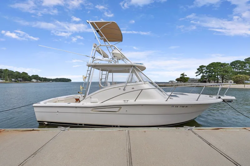 Slide: The Image of 1995 Pursuit 3000 Offshore boat docked by a scenic waterfront under a clear blue sky. - 46