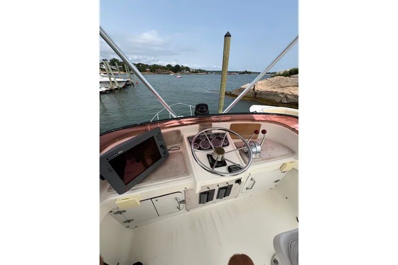 Slide: The Image of 1974 Bertram 31 Flybridge Cruiser helm with steering wheel and navigation equipment, overlooking serene waters. - 23