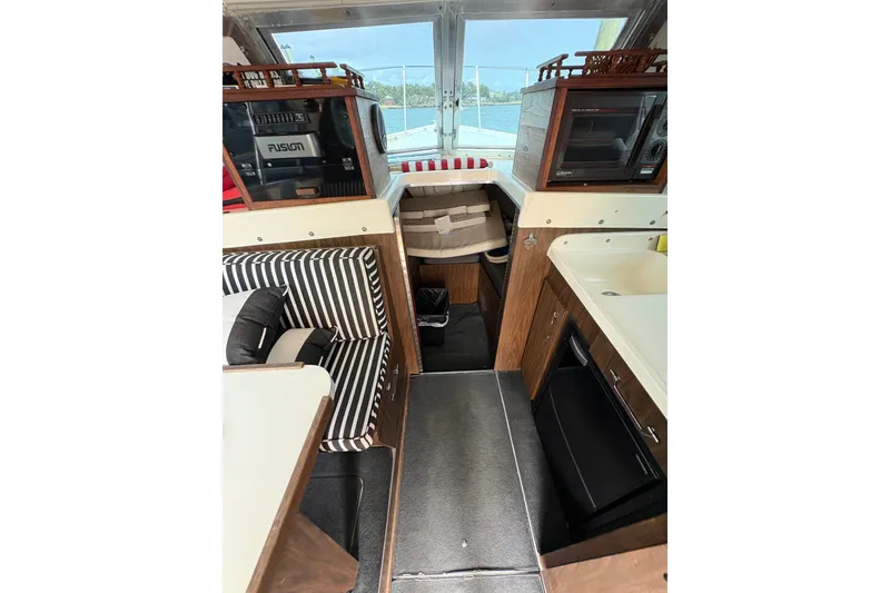 Slide: The Image of 1974 Bertram 31 Flybridge Cruiser interior with striped seating, compact kitchen, and scenic window view. - 28