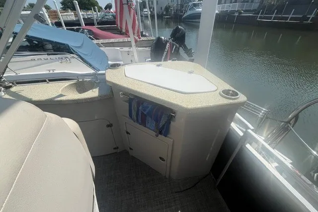 Slide: The Image of 2018 Harris Solstice 220 boat interior with sink and storage, docked by calm waters. - 23