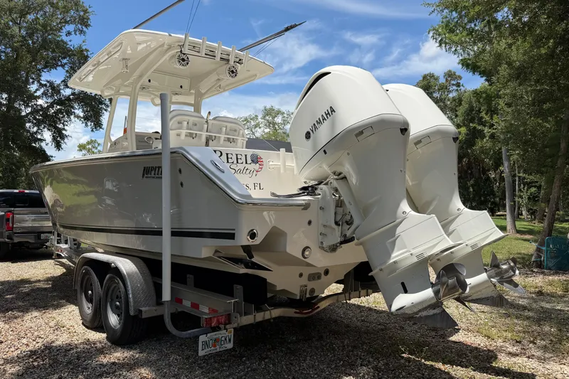 Slide: The Image of 2019 Jupiter 30 boat with dual Yamaha engines on a trailer in a wooded area. - 6