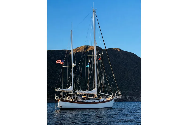 Slide: The Image of 1977 Hans Christian Ketch sailboat anchored near scenic coastal cliffs. - 2